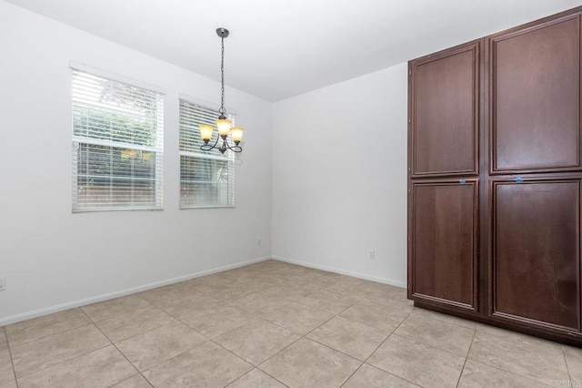 unfurnished dining area featuring light tile patterned floors, baseboards, and an inviting chandelier