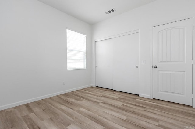 unfurnished bedroom with light wood finished floors, visible vents, a closet, and baseboards