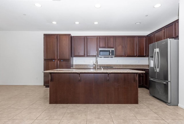 kitchen featuring light stone counters, light tile patterned flooring, a center island with sink, and stainless steel appliances