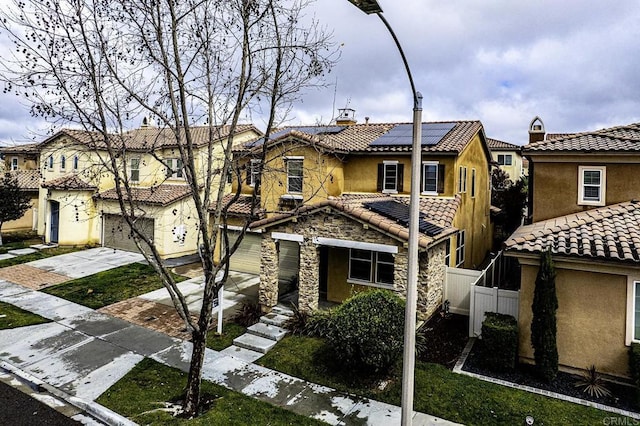 multi unit property featuring a tile roof, fence, roof mounted solar panels, and stucco siding