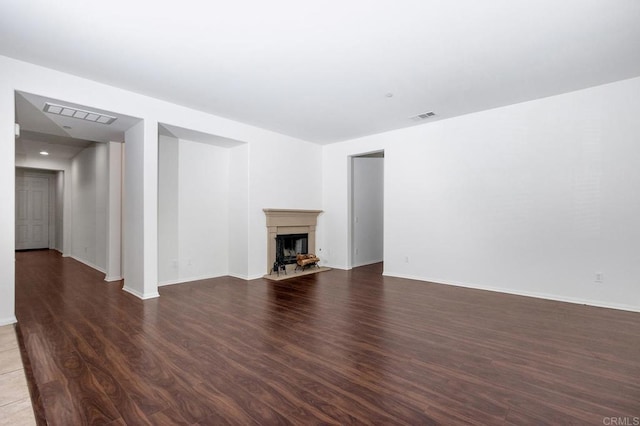 unfurnished living room featuring a fireplace with flush hearth, wood finished floors, visible vents, and baseboards