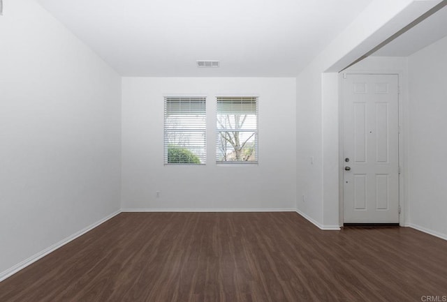 unfurnished room featuring visible vents, baseboards, and dark wood finished floors