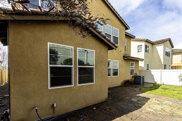 view of side of property featuring fence, central air condition unit, a tiled roof, stucco siding, and a patio area