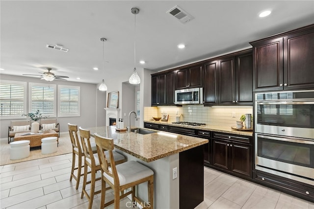 kitchen with light stone countertops, visible vents, a sink, decorative backsplash, and appliances with stainless steel finishes