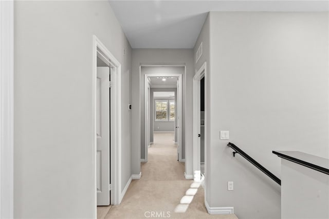 corridor featuring an upstairs landing, light colored carpet, and baseboards