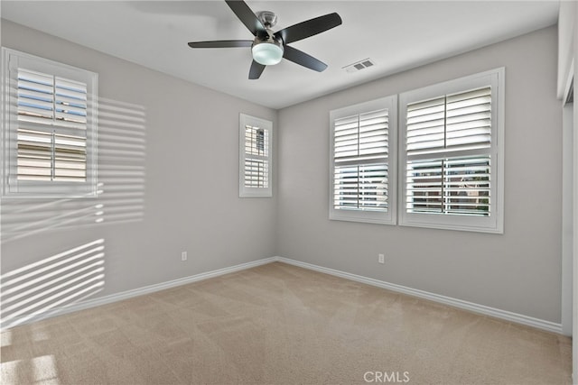 empty room with baseboards, visible vents, a ceiling fan, and carpet