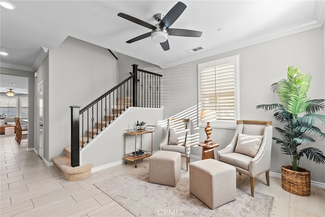 sitting room with visible vents, crown molding, stairs, and a ceiling fan