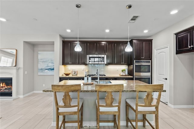 kitchen featuring visible vents, backsplash, light stone countertops, a breakfast bar area, and appliances with stainless steel finishes