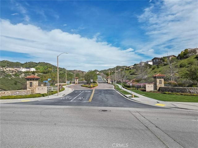 view of road with street lights, curbs, sidewalks, and a gated entry