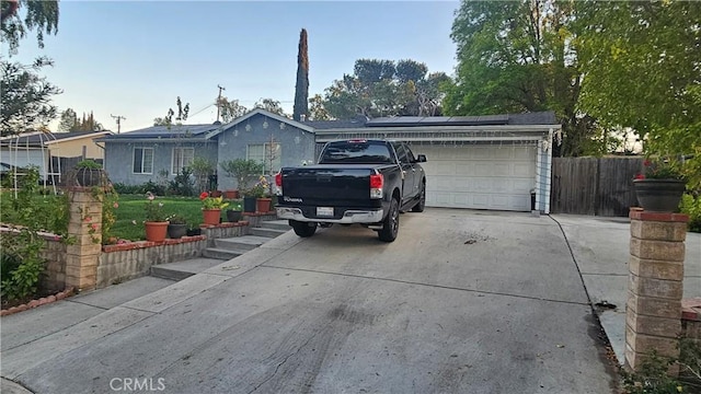 single story home with stucco siding, roof mounted solar panels, fence, concrete driveway, and a garage