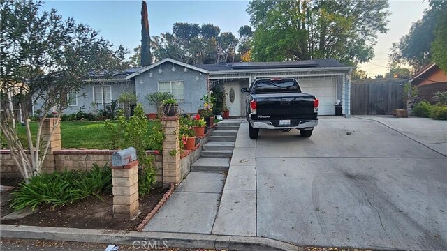 ranch-style home featuring an attached garage, solar panels, driveway, and fence