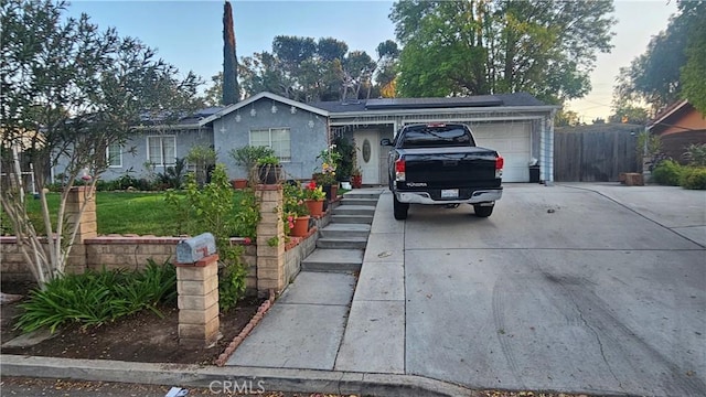 ranch-style home featuring a garage, roof mounted solar panels, concrete driveway, and fence