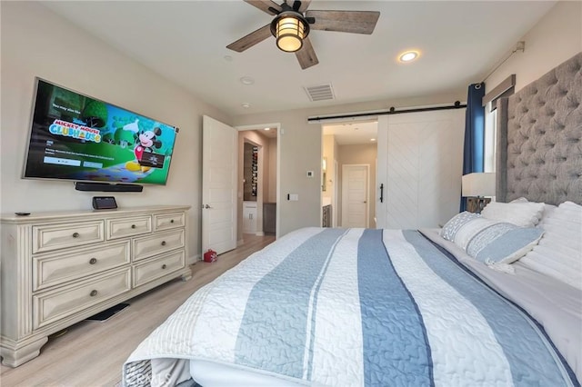 bedroom with a ceiling fan, visible vents, light wood finished floors, ensuite bath, and a barn door