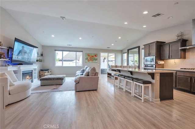 living room with visible vents, light wood-style flooring, a glass covered fireplace, recessed lighting, and lofted ceiling