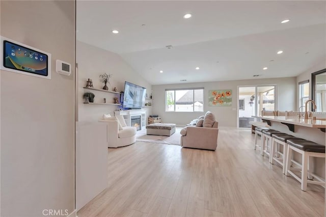 living area featuring a glass covered fireplace, vaulted ceiling, recessed lighting, and light wood-type flooring