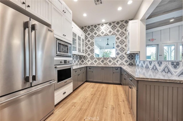 kitchen featuring visible vents, gray cabinetry, light stone counters, appliances with stainless steel finishes, and decorative backsplash