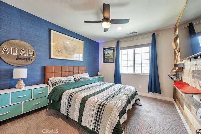 carpeted bedroom with an accent wall, baseboards, visible vents, and ceiling fan