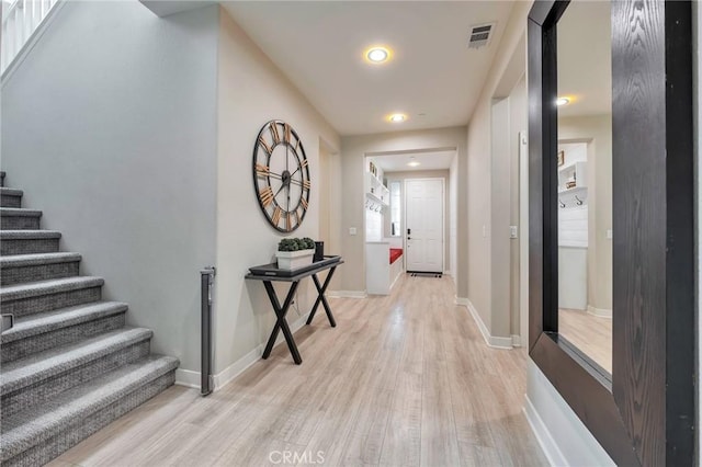 corridor with visible vents, baseboards, stairs, and light wood finished floors