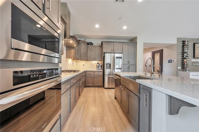 kitchen with light stone counters, a sink, decorative backsplash, stainless steel appliances, and light wood-type flooring