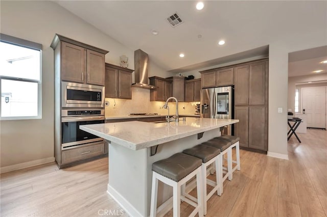 kitchen featuring visible vents, a sink, decorative backsplash, stainless steel appliances, and wall chimney exhaust hood