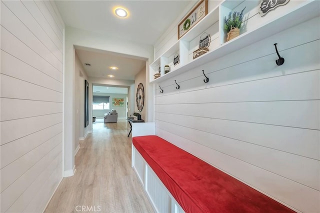 mudroom featuring baseboards, wooden walls, and light wood finished floors