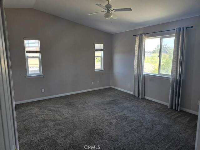 spare room featuring baseboards, ceiling fan, dark carpet, and vaulted ceiling