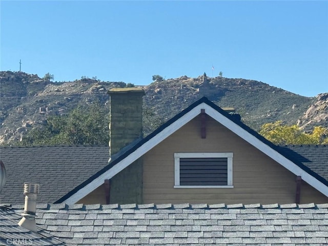 view of side of home with a chimney, a mountain view, and a shingled roof