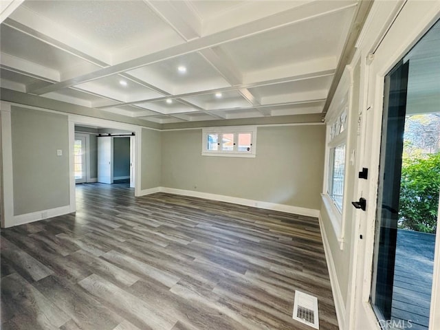 empty room with a barn door, wood finished floors, visible vents, and baseboards