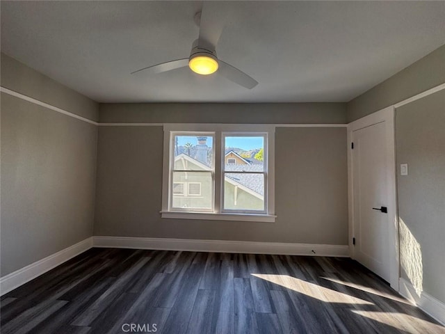 unfurnished room featuring baseboards, dark wood-type flooring, and ceiling fan