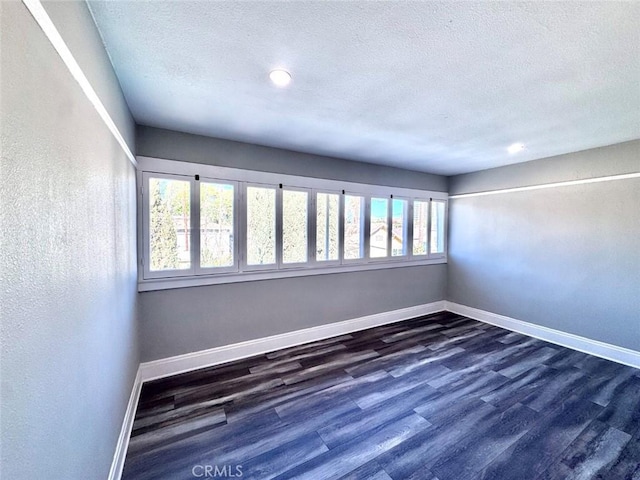 spare room with a textured ceiling, dark wood-type flooring, and baseboards