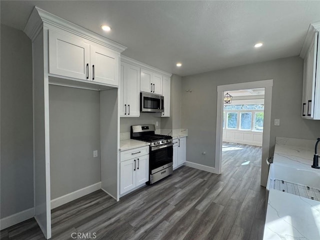 kitchen with light stone counters, dark wood-style floors, baseboards, appliances with stainless steel finishes, and white cabinetry