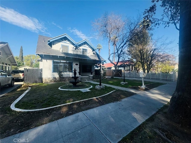 bungalow-style home with a balcony, a front yard, and fence