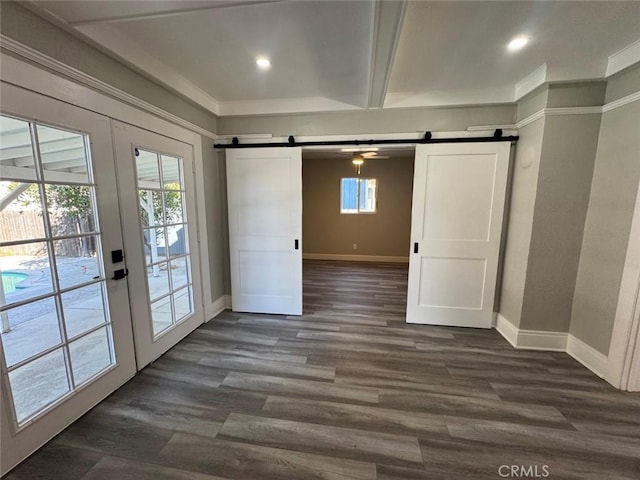 empty room with a barn door, a healthy amount of sunlight, dark wood-style floors, and french doors