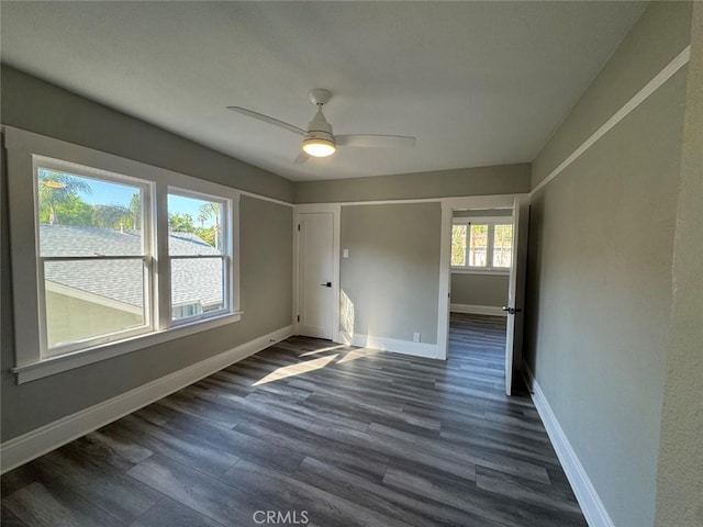 spare room with dark wood finished floors, a ceiling fan, and baseboards