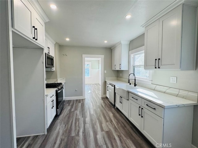 kitchen featuring baseboards, dark wood finished floors, a sink, appliances with stainless steel finishes, and white cabinetry