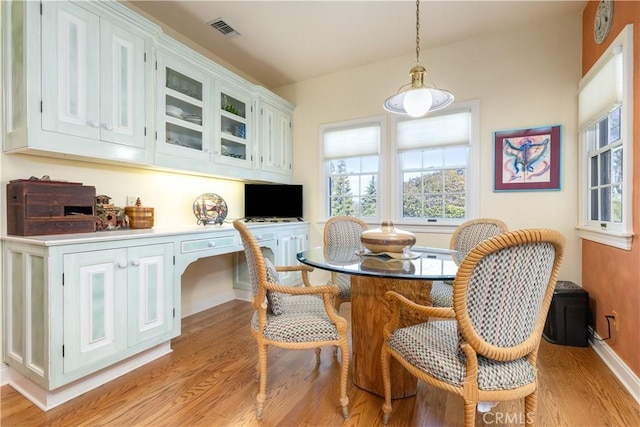 dining space with light wood-type flooring, baseboards, visible vents, and built in study area