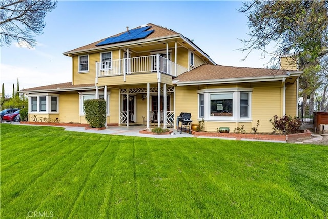 back of property with a lawn, a patio, a balcony, solar panels, and a chimney