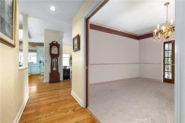 hallway featuring a chandelier, ornamental molding, baseboards, and wood finished floors