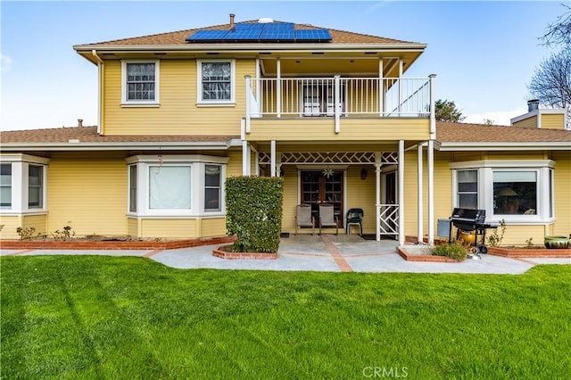 rear view of house featuring a chimney, a balcony, solar panels, and a lawn