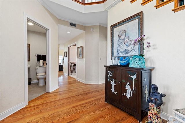 corridor with visible vents, crown molding, light wood-type flooring, and baseboards