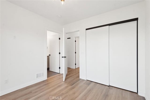 unfurnished bedroom featuring light wood finished floors, visible vents, baseboards, and a closet