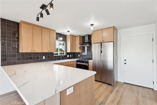 kitchen with range with gas stovetop, a peninsula, freestanding refrigerator, a sink, and wall chimney range hood