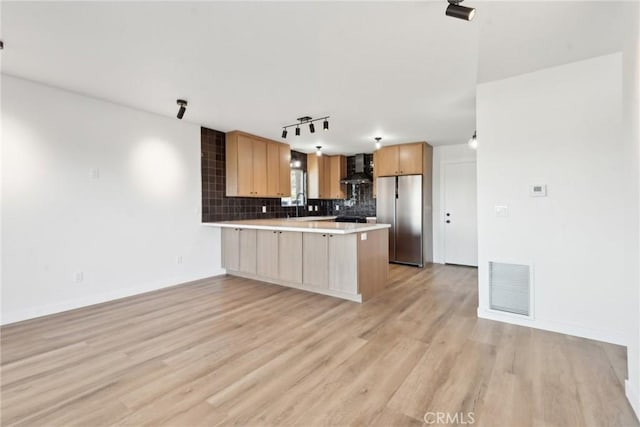 kitchen with visible vents, backsplash, wall chimney range hood, a peninsula, and freestanding refrigerator