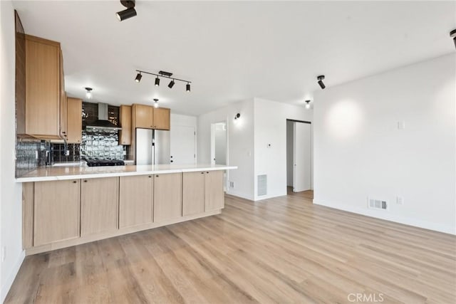 kitchen featuring visible vents, a peninsula, freestanding refrigerator, light countertops, and wall chimney exhaust hood