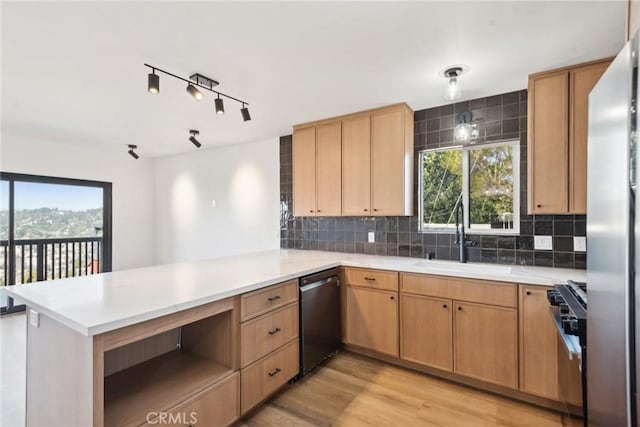 kitchen featuring a peninsula, a sink, stainless steel appliances, light countertops, and light wood-type flooring