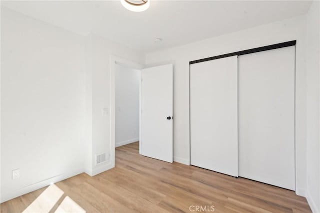 unfurnished bedroom featuring visible vents, baseboards, a closet, and light wood finished floors