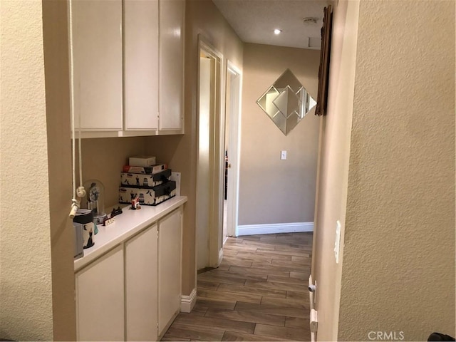 hall featuring wood finish floors, baseboards, recessed lighting, and a textured wall