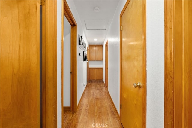 corridor featuring attic access, baseboards, and light wood finished floors