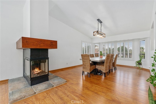 dining area featuring a multi sided fireplace, baseboards, high vaulted ceiling, and wood finished floors