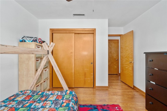 bedroom with a closet, visible vents, baseboards, and wood finished floors